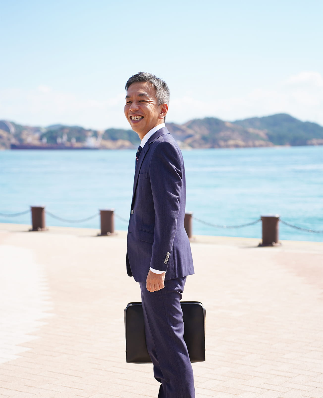 玉野市宇野港の瀬戸内の美しい海と自然をバックに笑顔で写る事務所代表